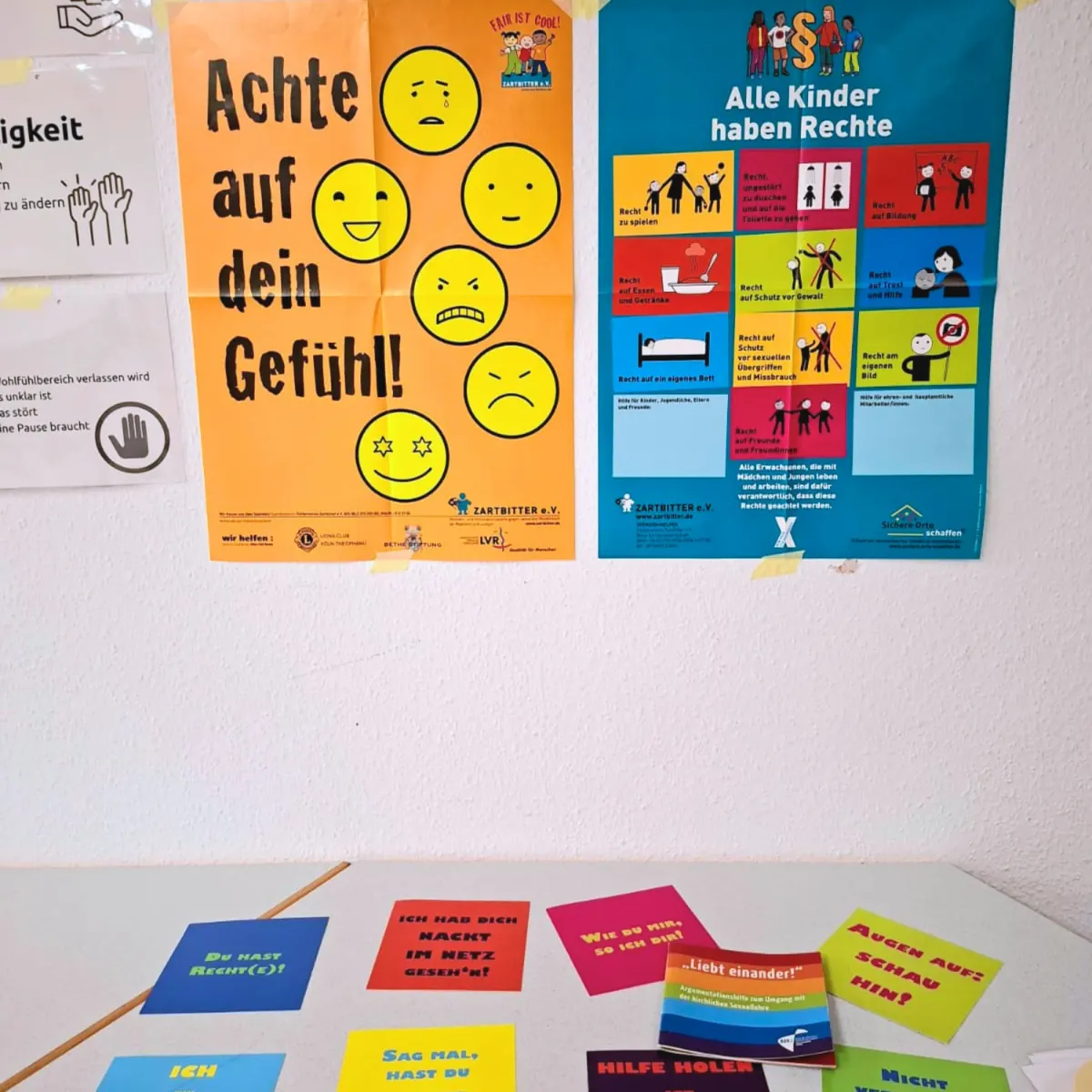 Zwei Präventionsplakate an einer Wand, „Achte auf dein Gefühl!“ und „Alle Kinder haben Rechte“, darunter bunte Karten auf einem Tisch